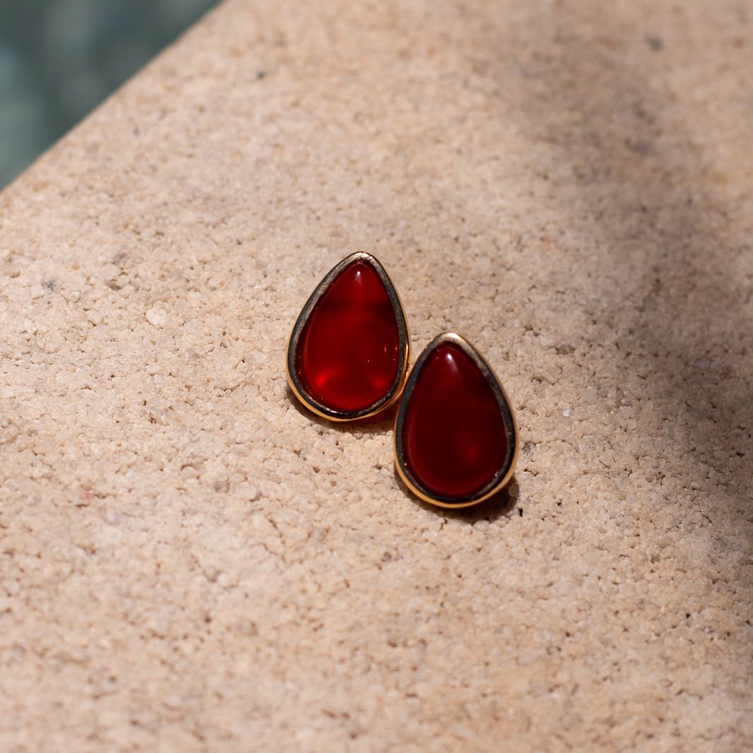 Red teardrop-shaped earrings on a beige surface with water in the background