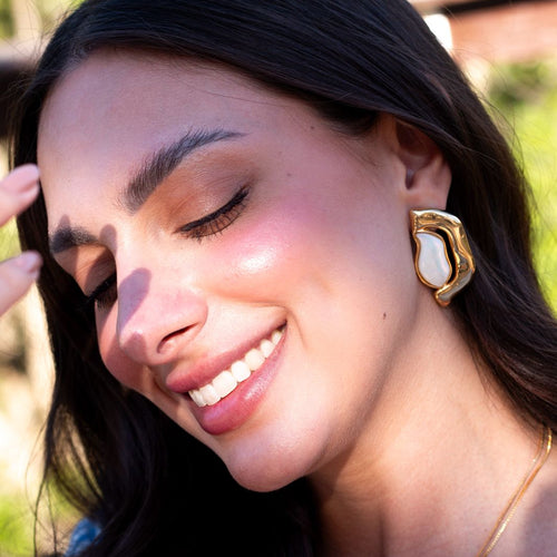 Woman wearing gold earrings with a blurred natural background