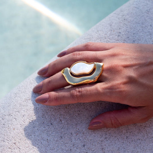 Hand wearing a gold and white ring on a light blue background