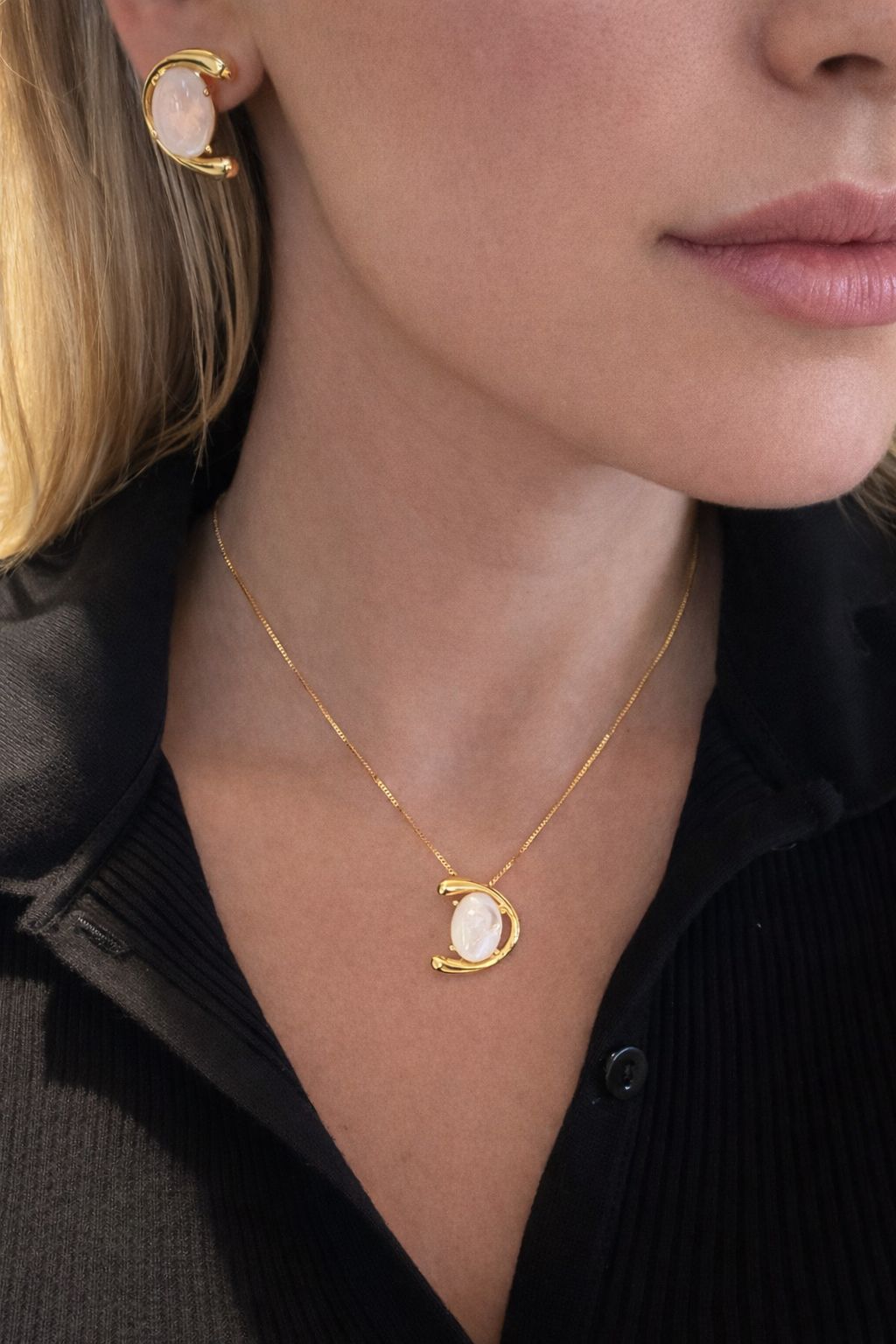 Close-up of a woman wearing a gold necklace and earring with a moon-phase pendant.
