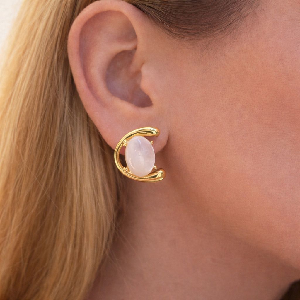 Gold earring with nacre gemstone worn by a person with blonde hair.