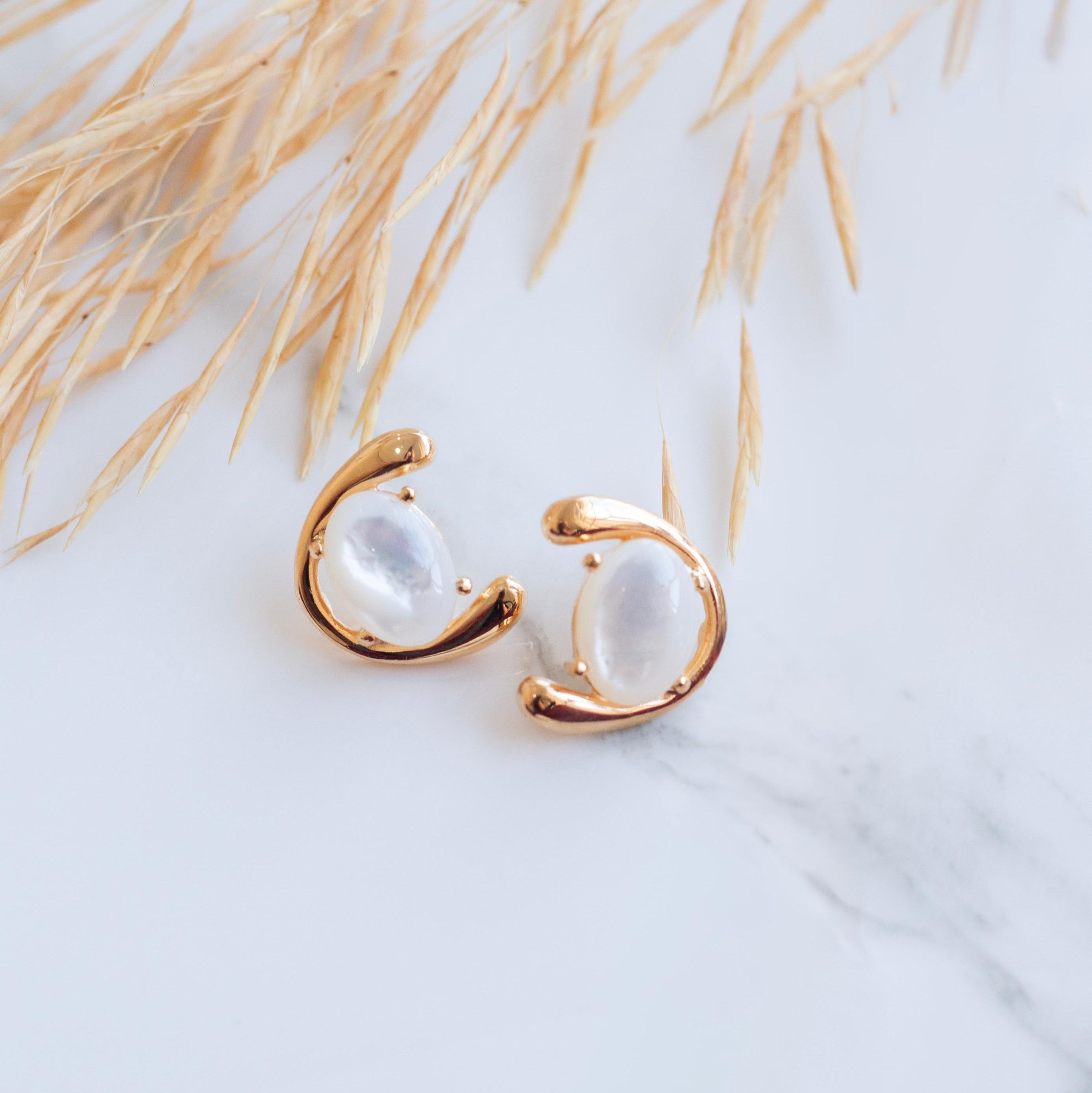 Gold earrings with nacre stones on a light background