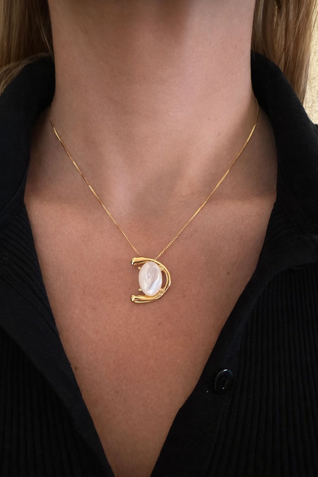 Gold necklace with a half-moon pendant and nacre gemstone worn by a woman