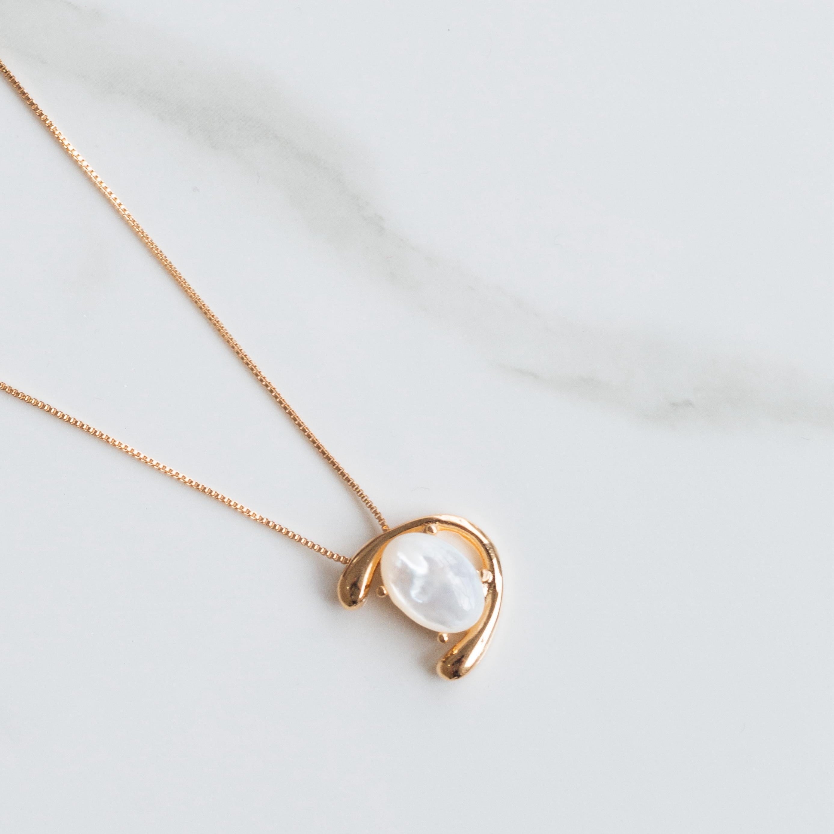 Necklace with a gold chain and nacre pendant on a white marble surface