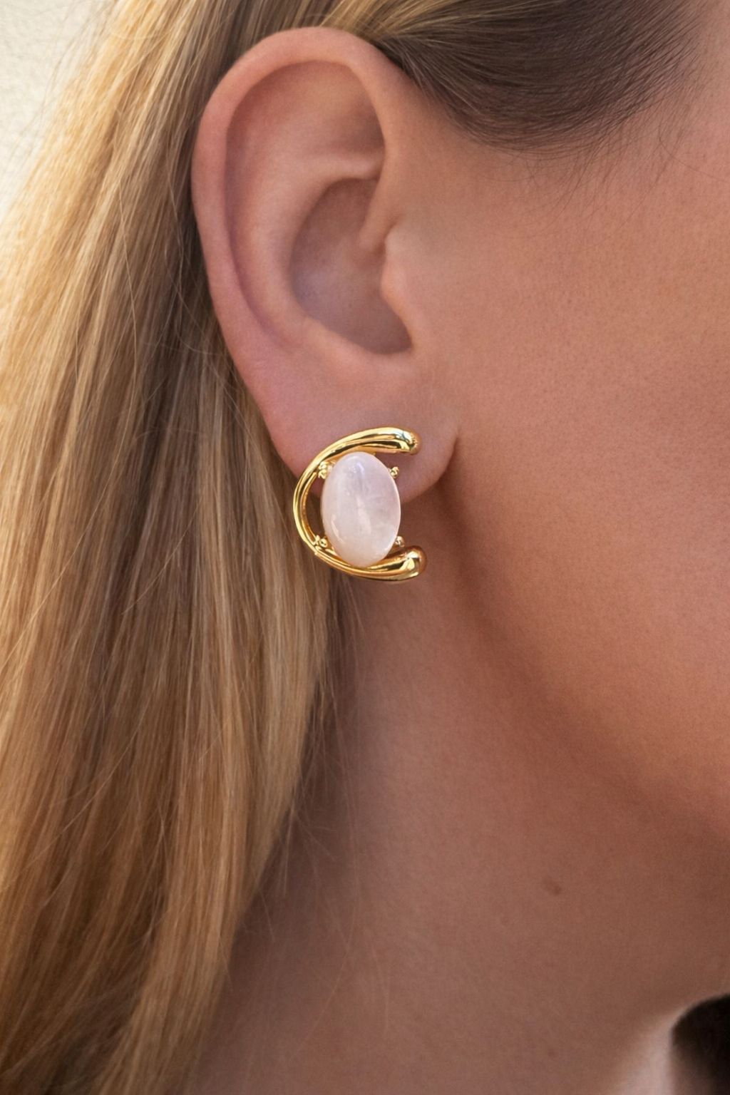 Gold earring with a nacre stone worn by a person