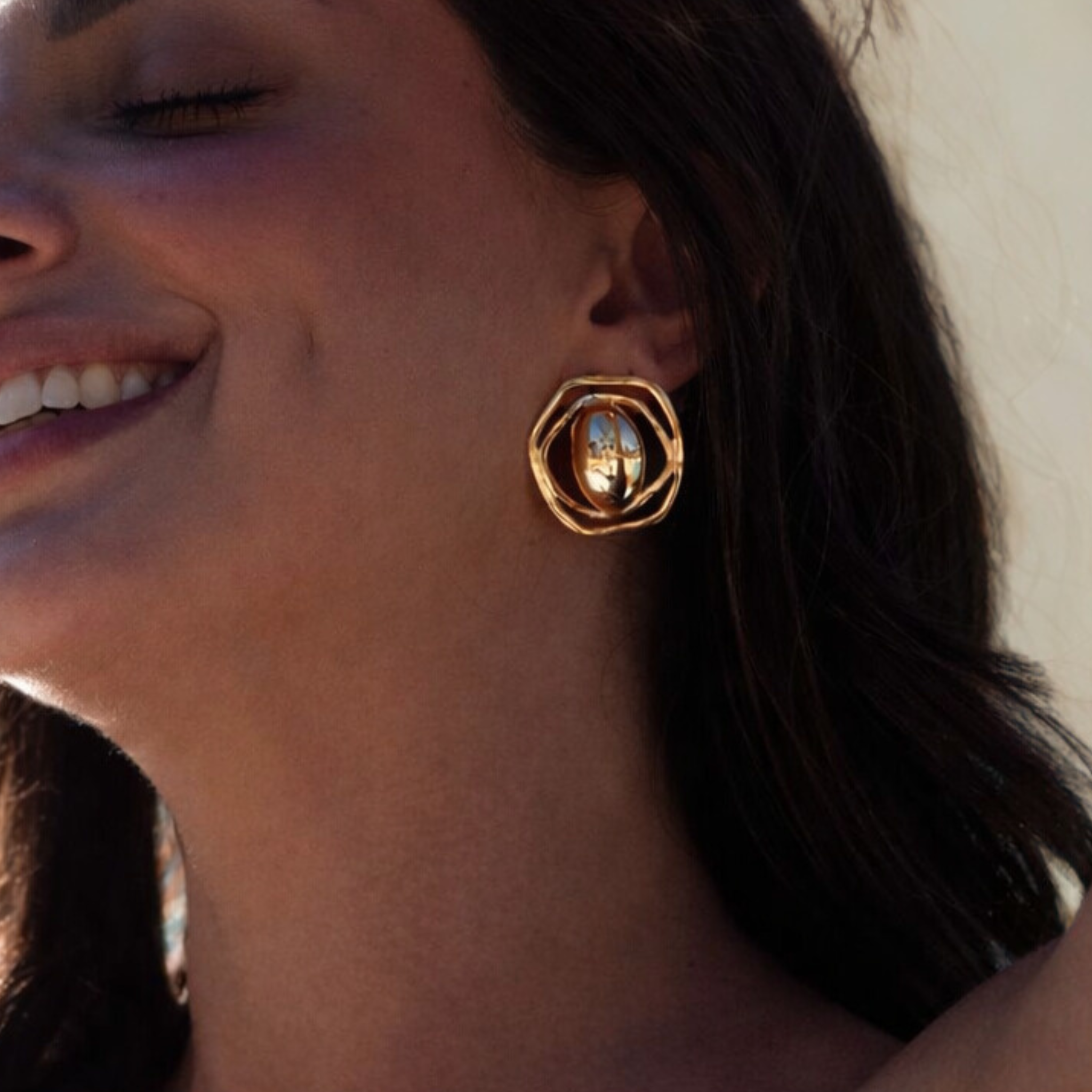 Close-up of a person wearing gold hoop earrings with a neutral background