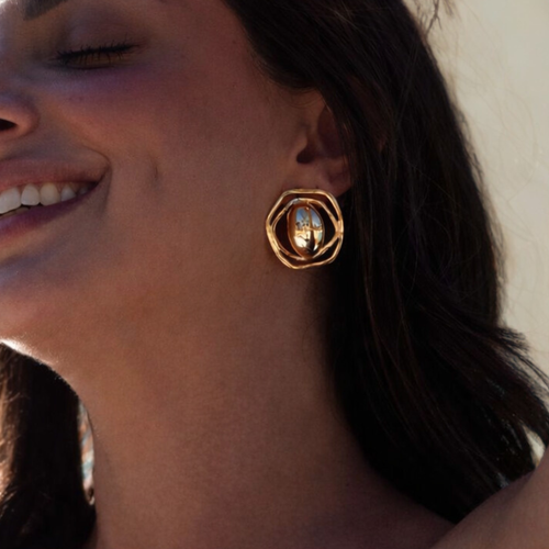 Close-up of a person wearing gold hoop earrings with a neutral background