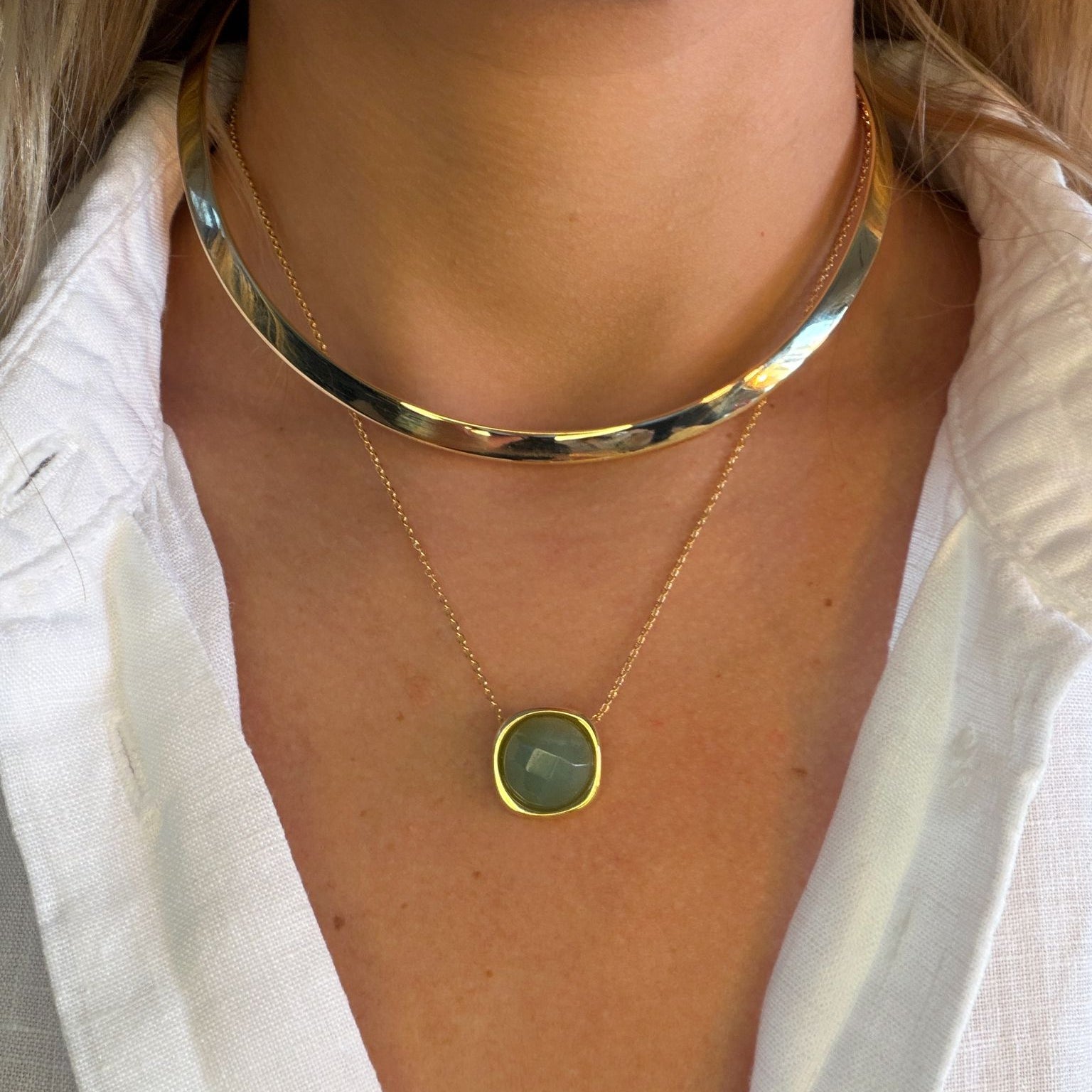 Gold collar and gold necklace with a green pendant worn by a person against a white background