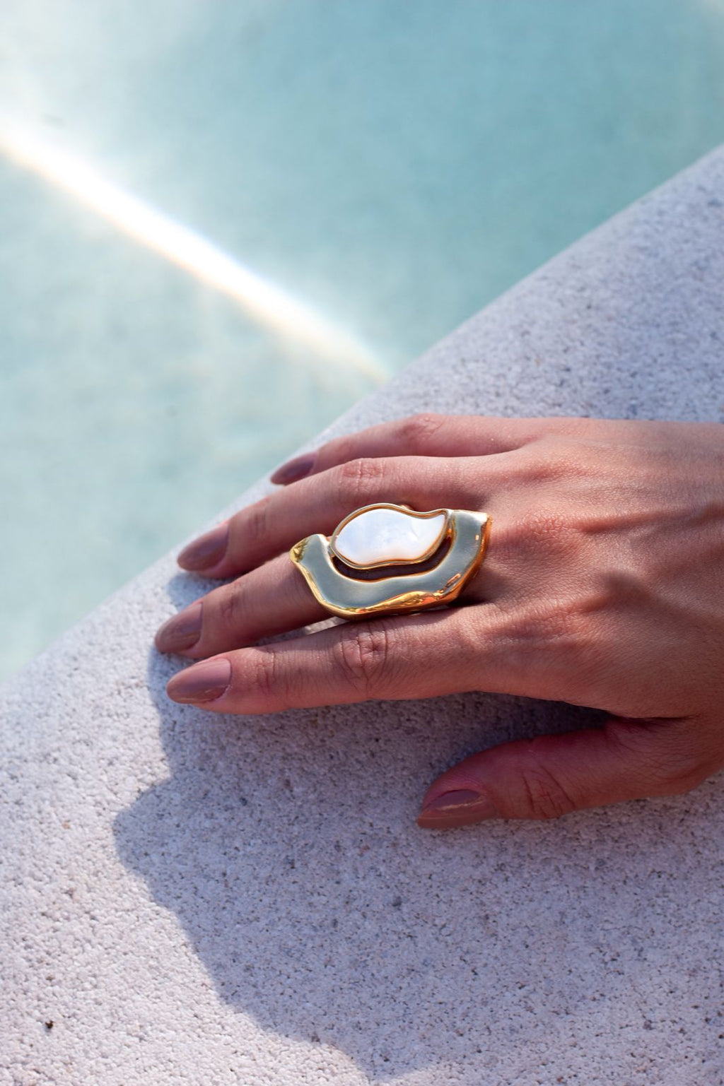 Hand wearing a gold and white ring on a light blue background