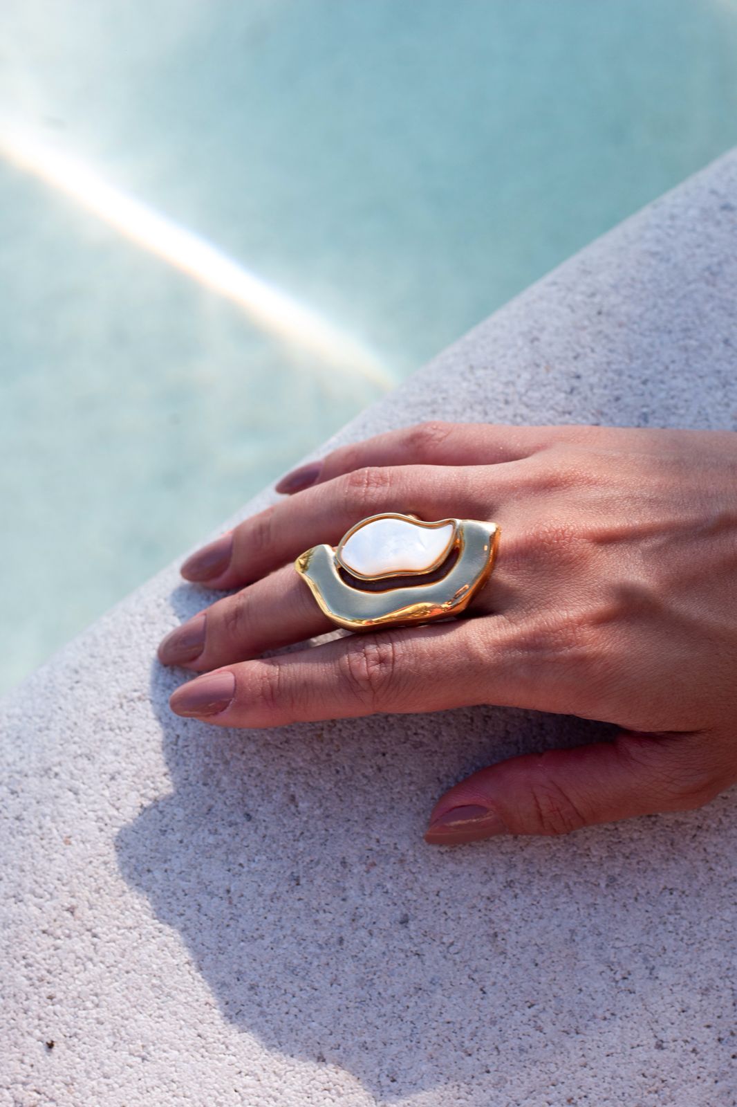 Hand wearing a gold and white ring on a light blue background