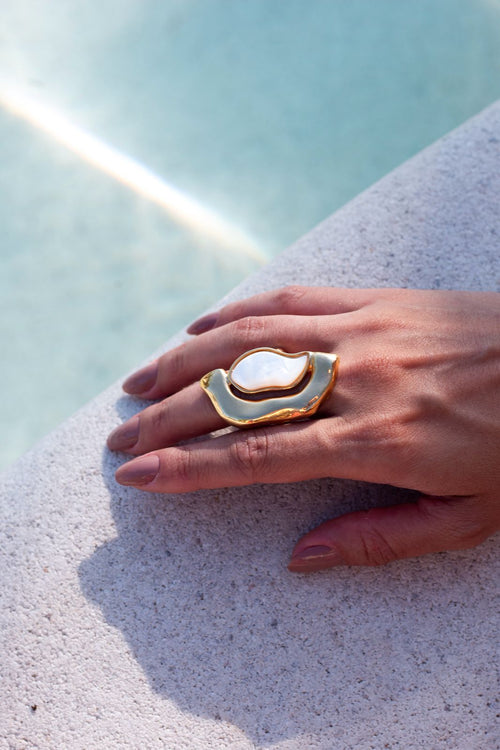 Hand wearing a gold and white ring on a light blue background