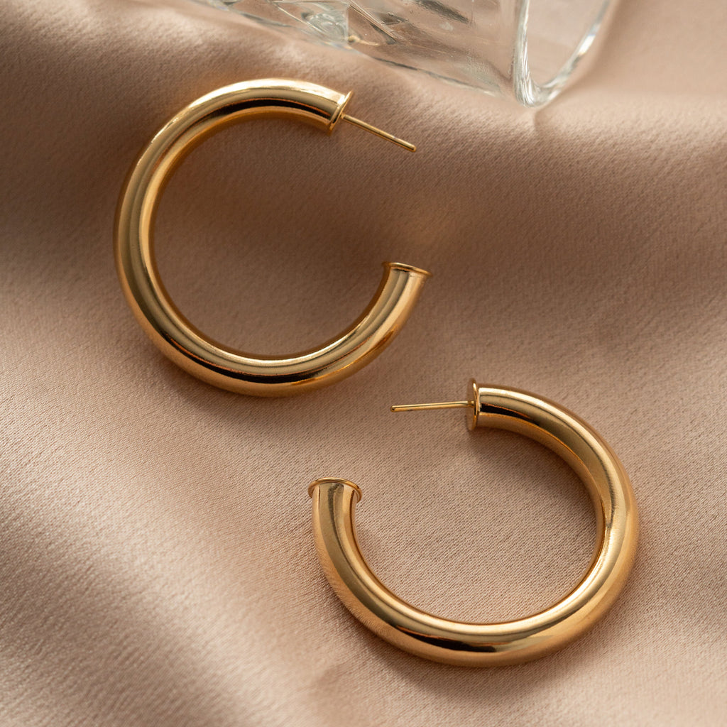 Gold hoop earrings on a beige fabric surface with a glass object in the background.