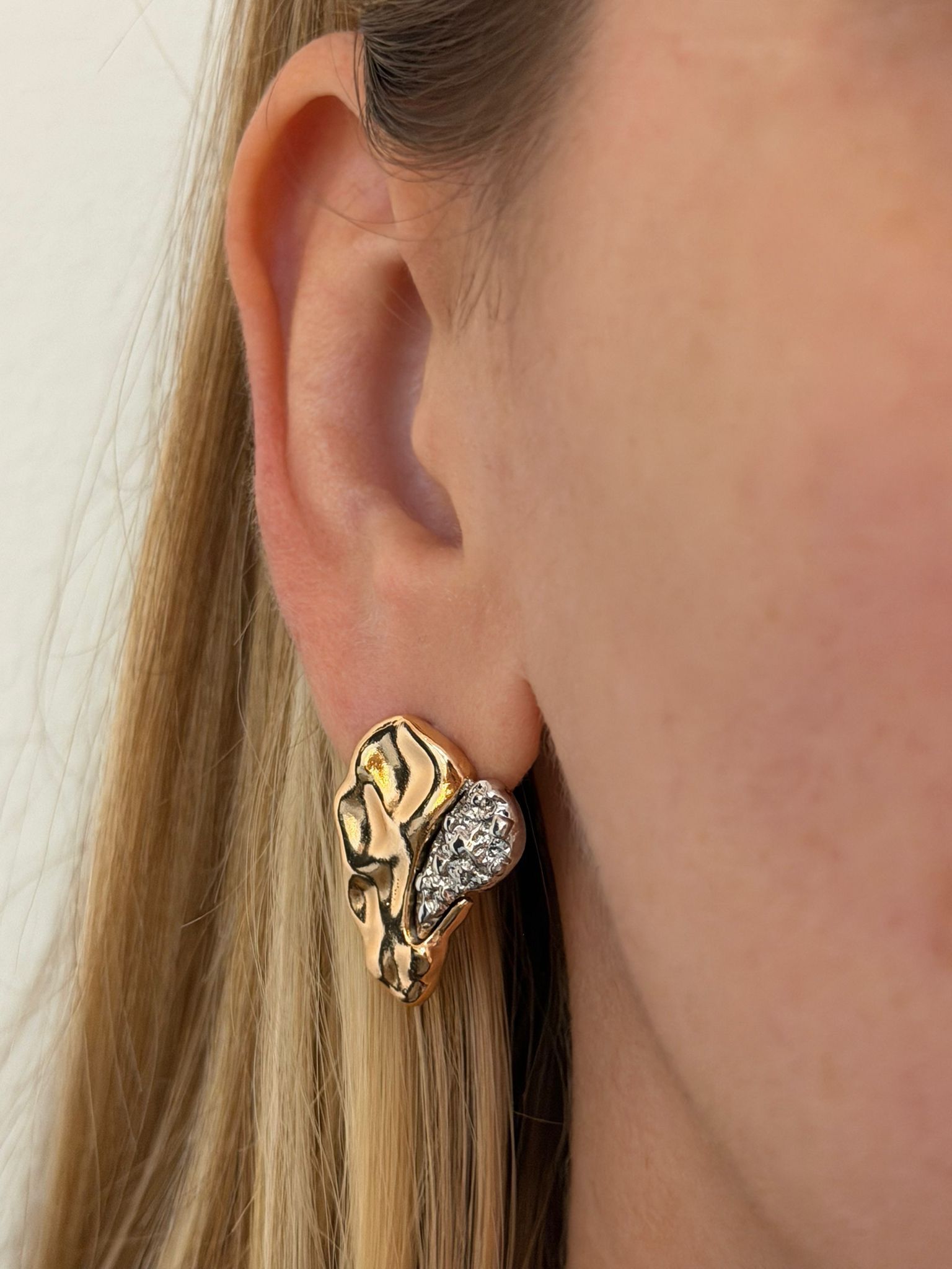 Gold earring worn by a person with blonde hair.