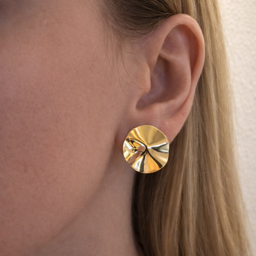 Close-up of a person wearing a gold round earring.