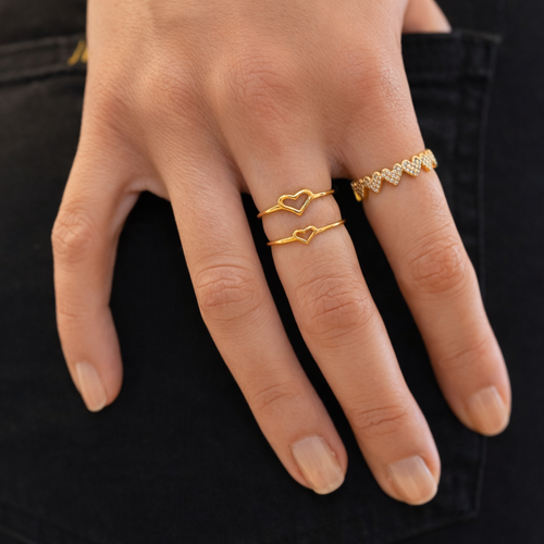 Hand wearing gold heart-shaped rings with a blurred background
