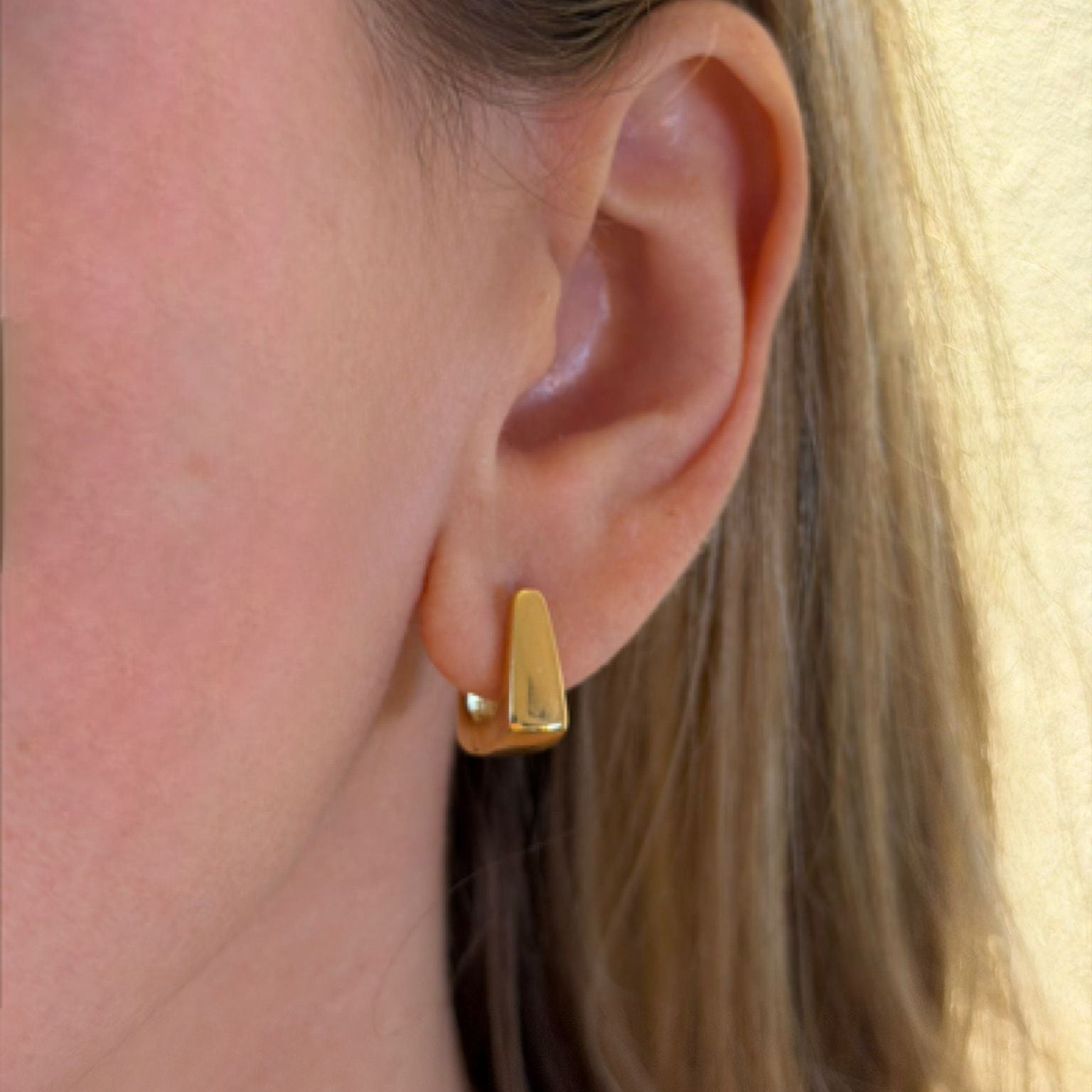 Close-up of an ear wearing a gold earring with a blurred background