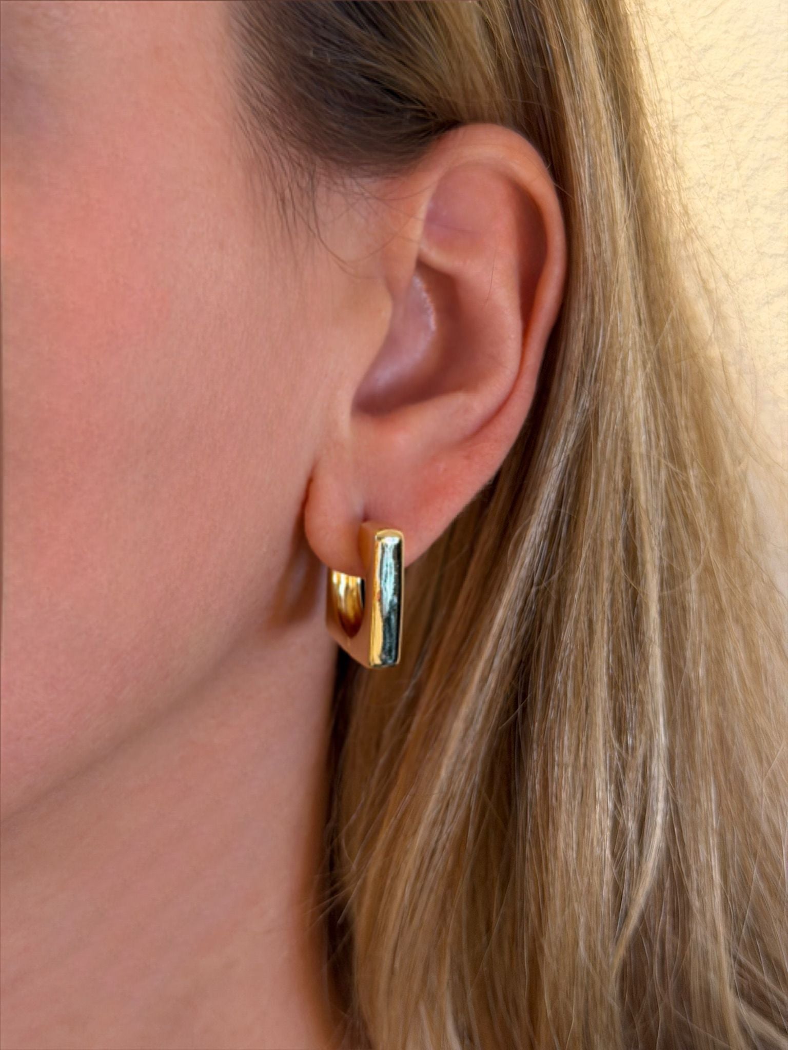 Close-up of a person wearing gold hoop  retangular earrings with a blurred background