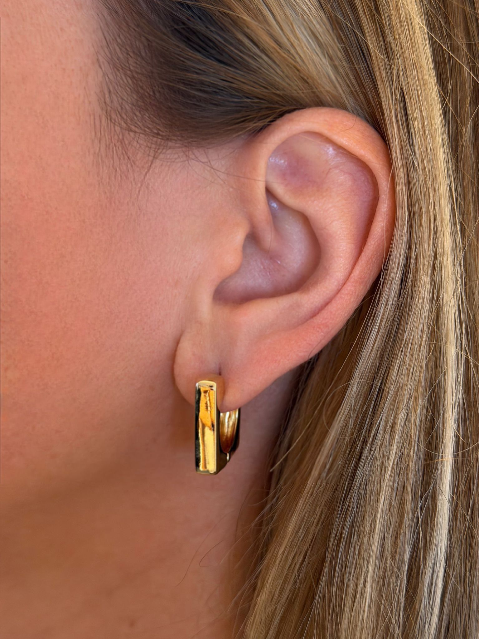Gold hoop retangular earring worn by a person with blonde hair.