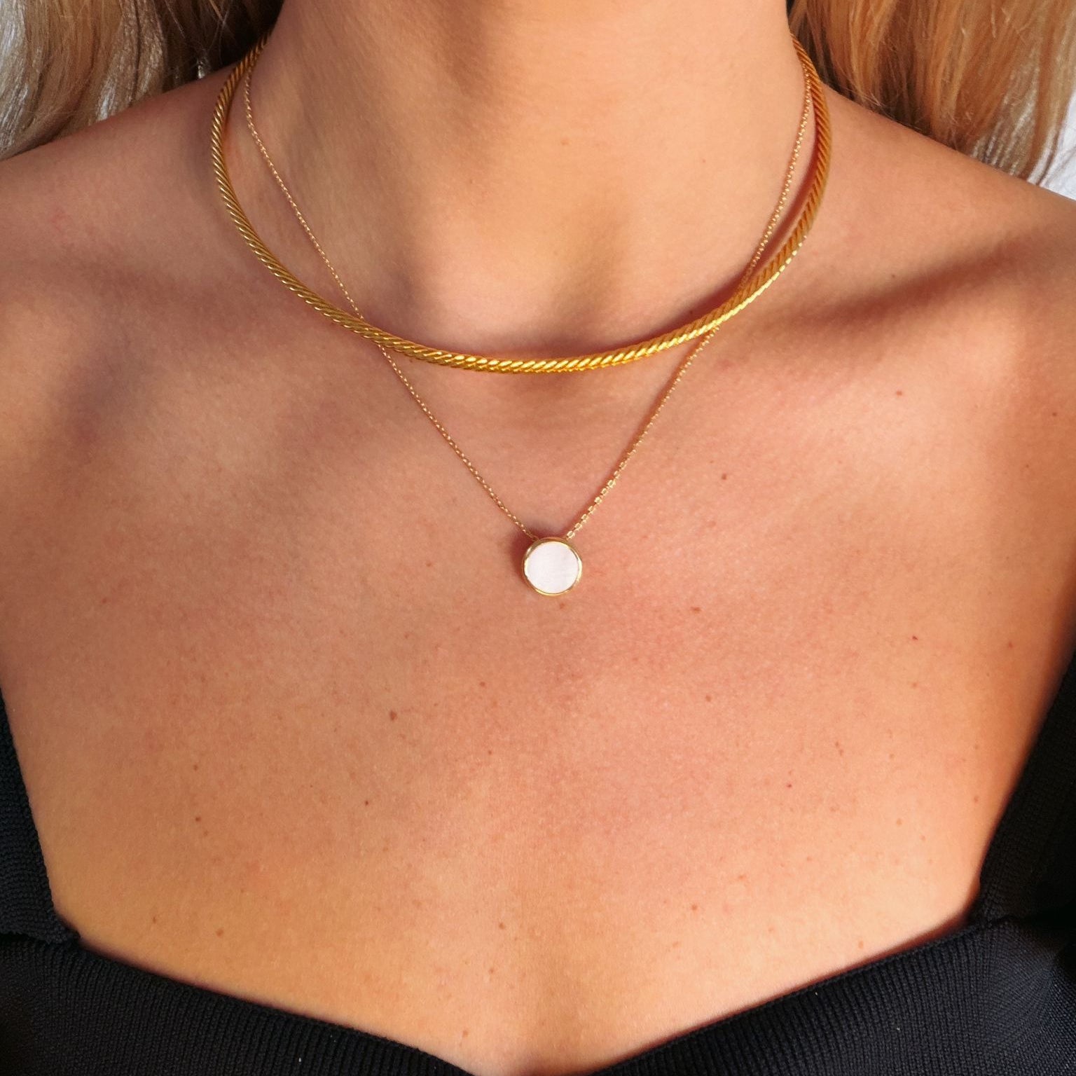Close-up of a person wearing a gold collar and a necklace with a round nacre pendant.