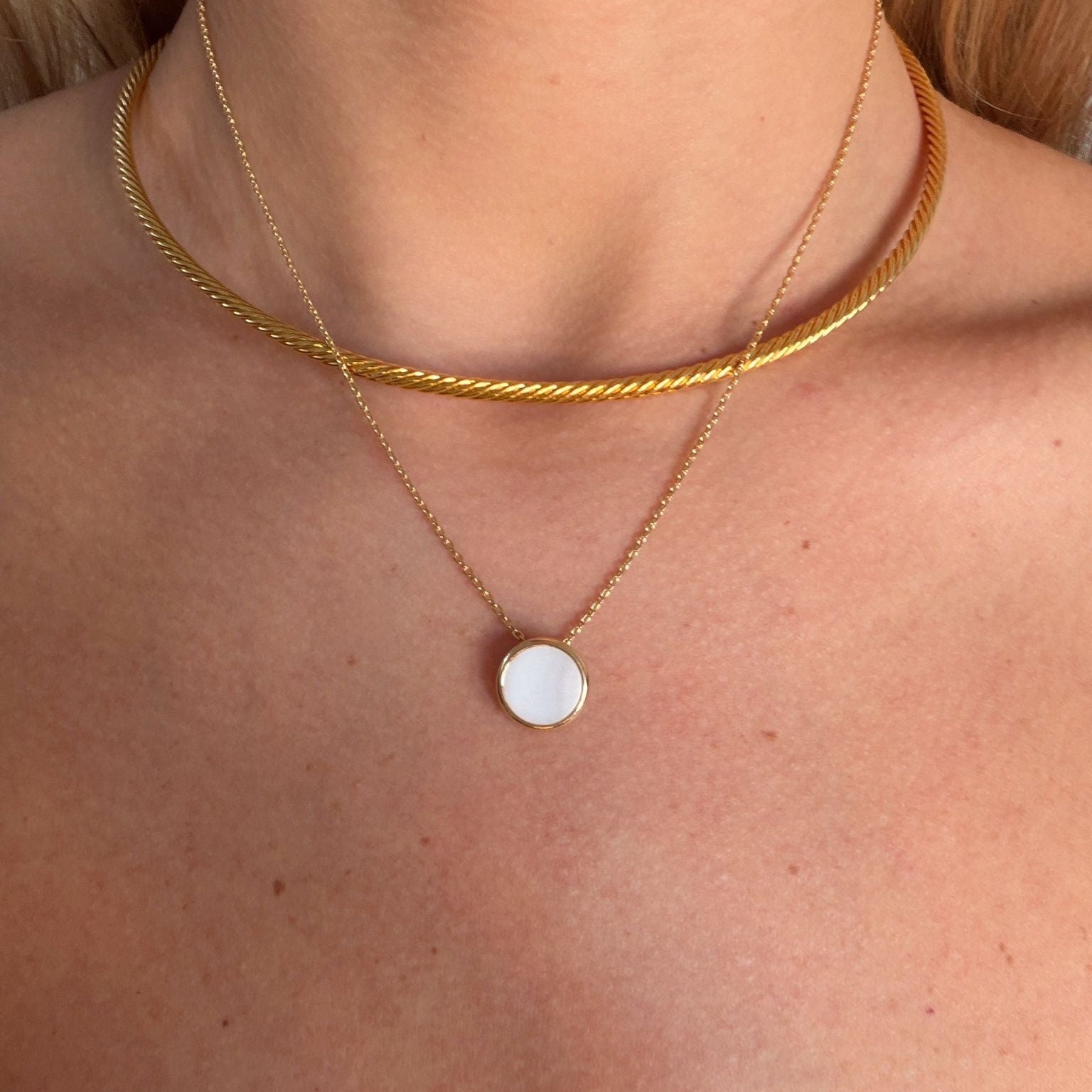 Gold collar and goldnecklace with a round nacre pendant on a person's neck