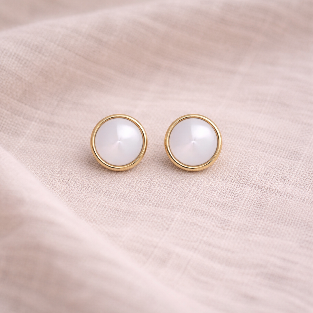 Pair of gold earrings with nacre gemstones on a soft pink fabric background