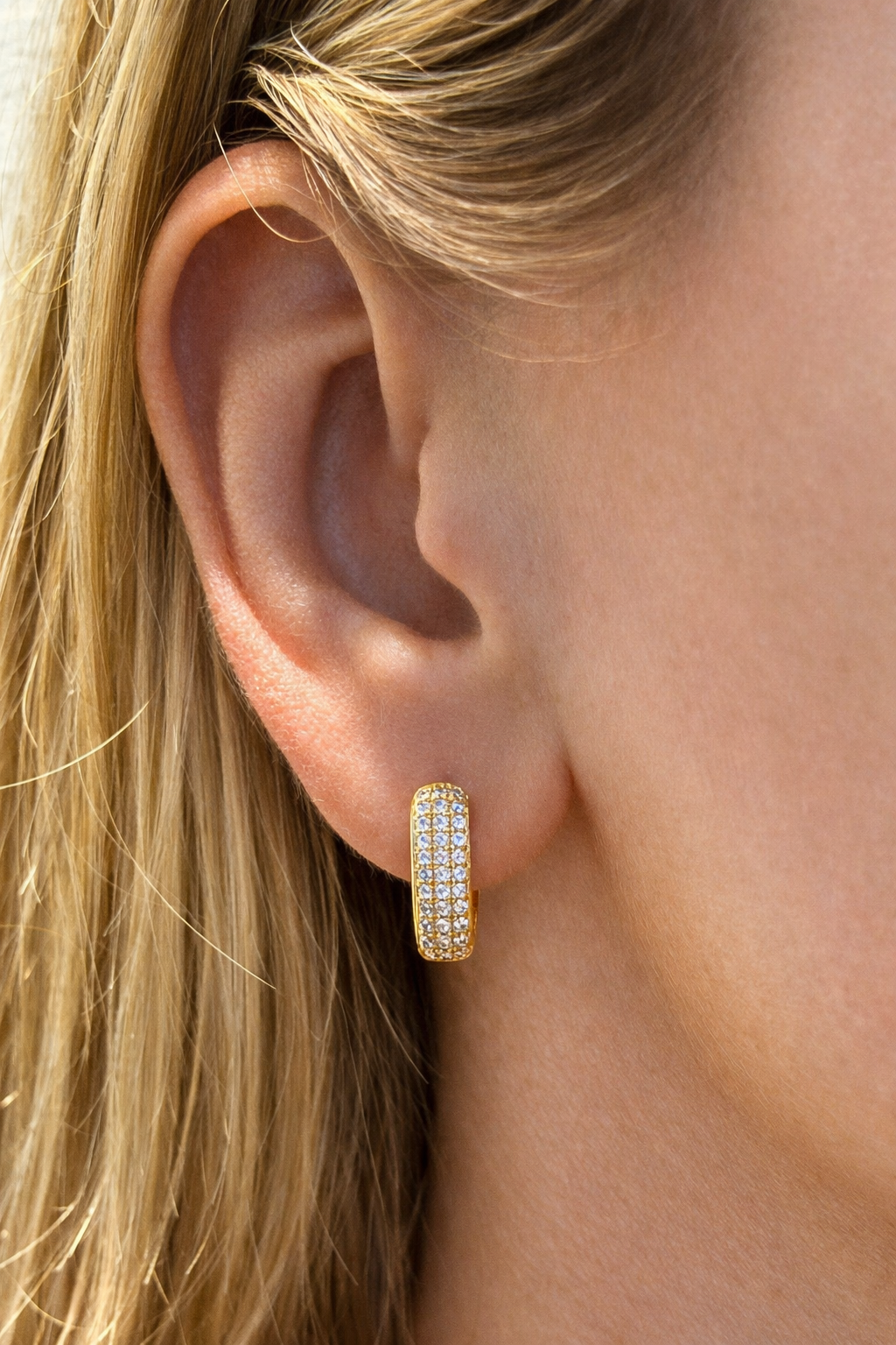 Close-up of a gold hoop earring worn by a person with blonde hair.