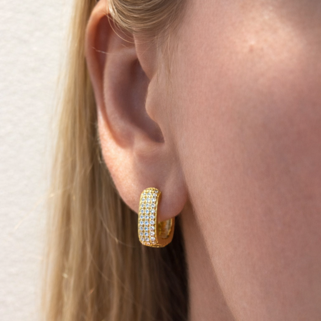 Gold Luz hoop earrings with clear gemstones worn by a person with blonde hair.