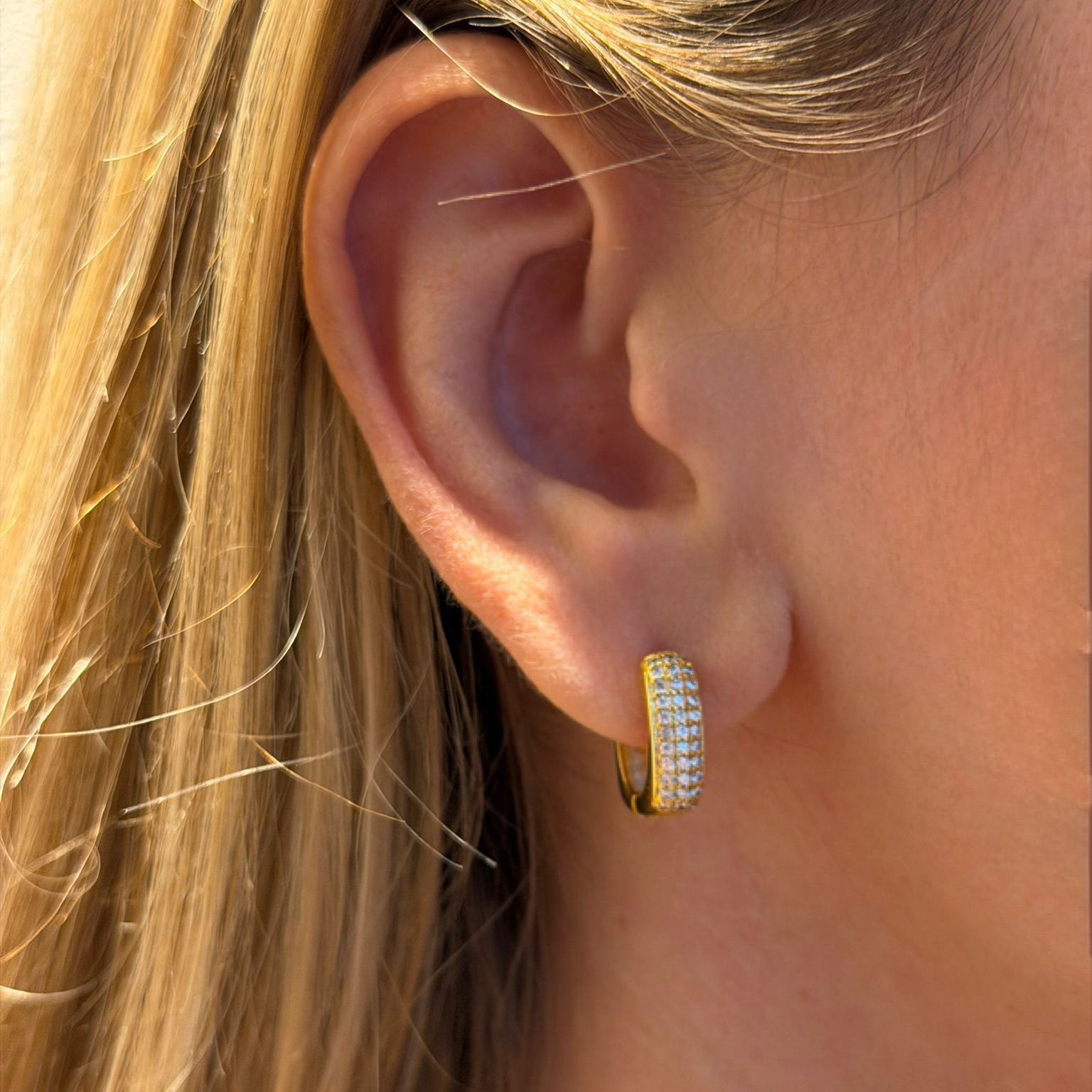Close-up of a person wearing gold hoop earrings with a blurred background