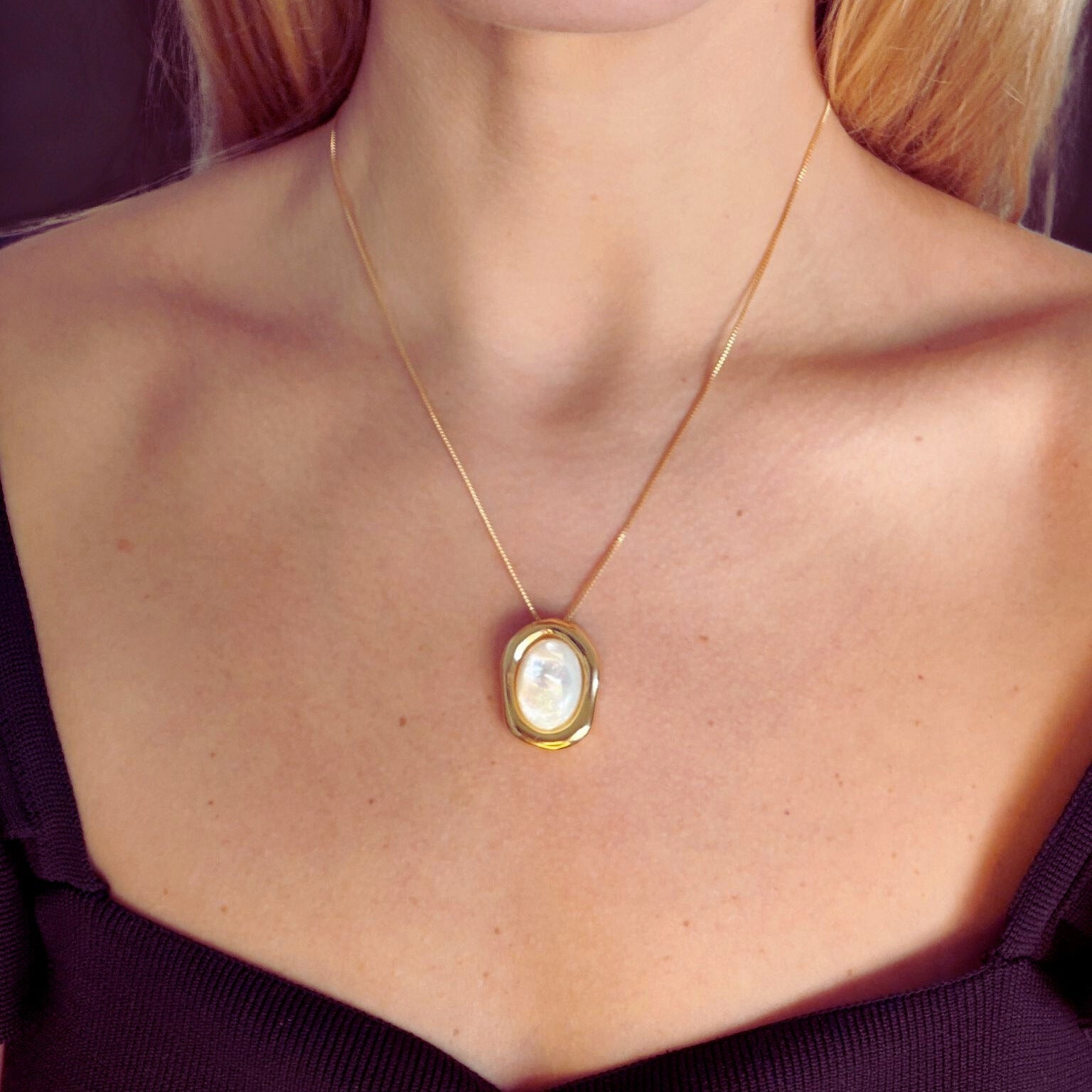 Gold necklace with a nacre pendant on a person wearing a dark top.