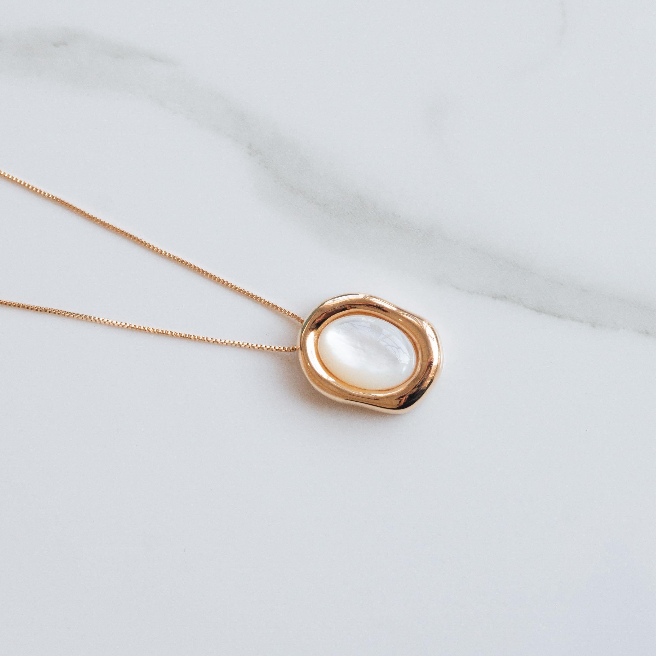 Gold necklace with a circular nacre pendant on a light gray background