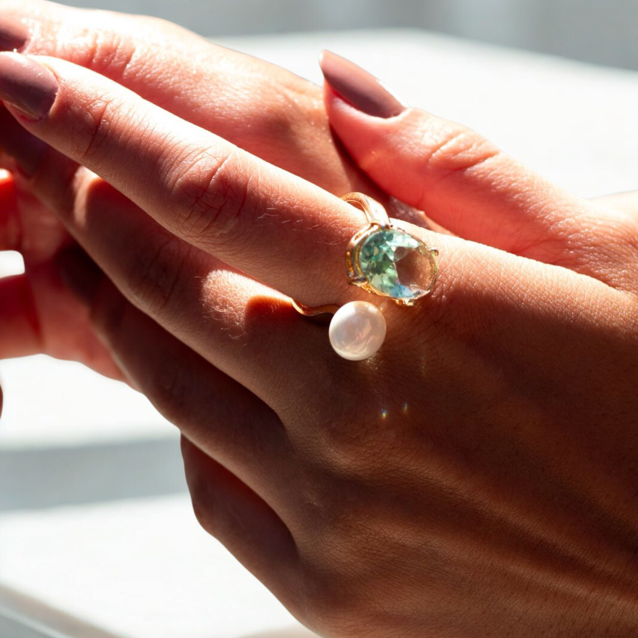 Close-up of a hand wearing a ring with a large gemstone and a pearl on a neutral background