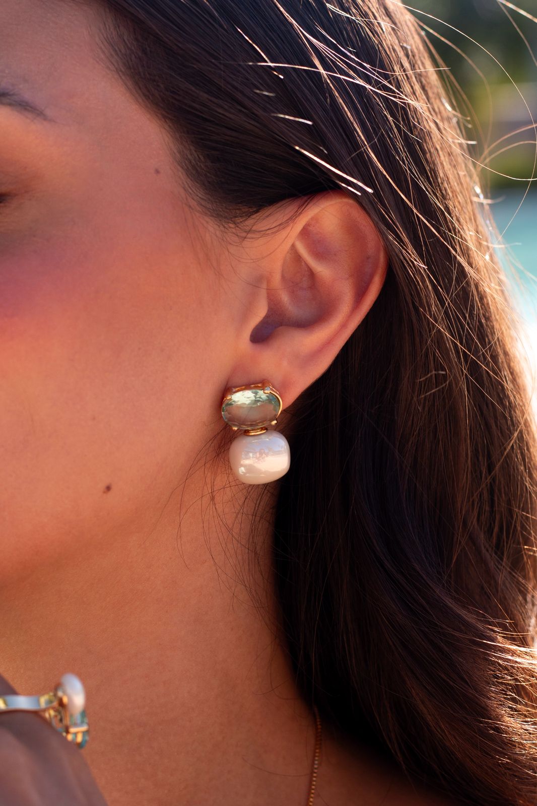 Close-up of a person wearing gold and pearl earrings with a blurred background