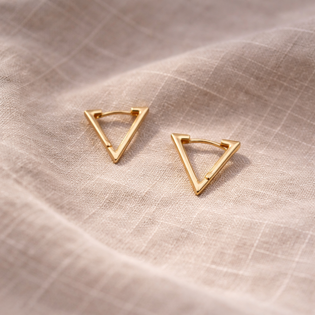 Gold triangle earrings on a beige fabric background
