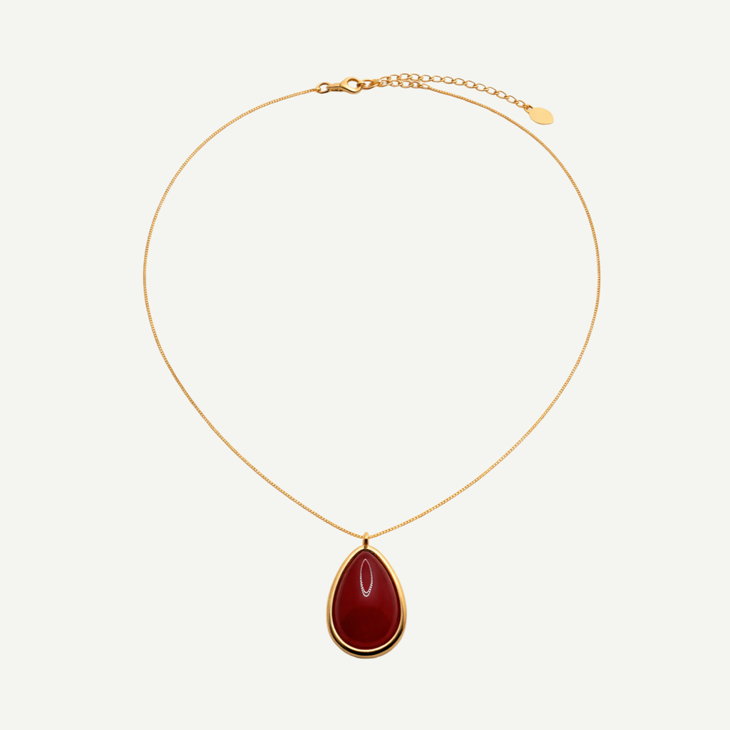 Gold necklace with a red natural agate teardrop pendant on a white background