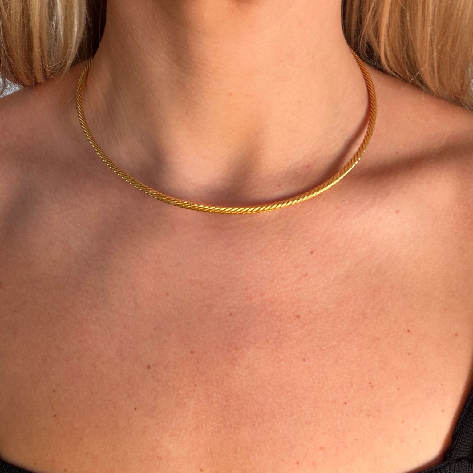 Close-up of a person wearing a gold collar and a black blouse