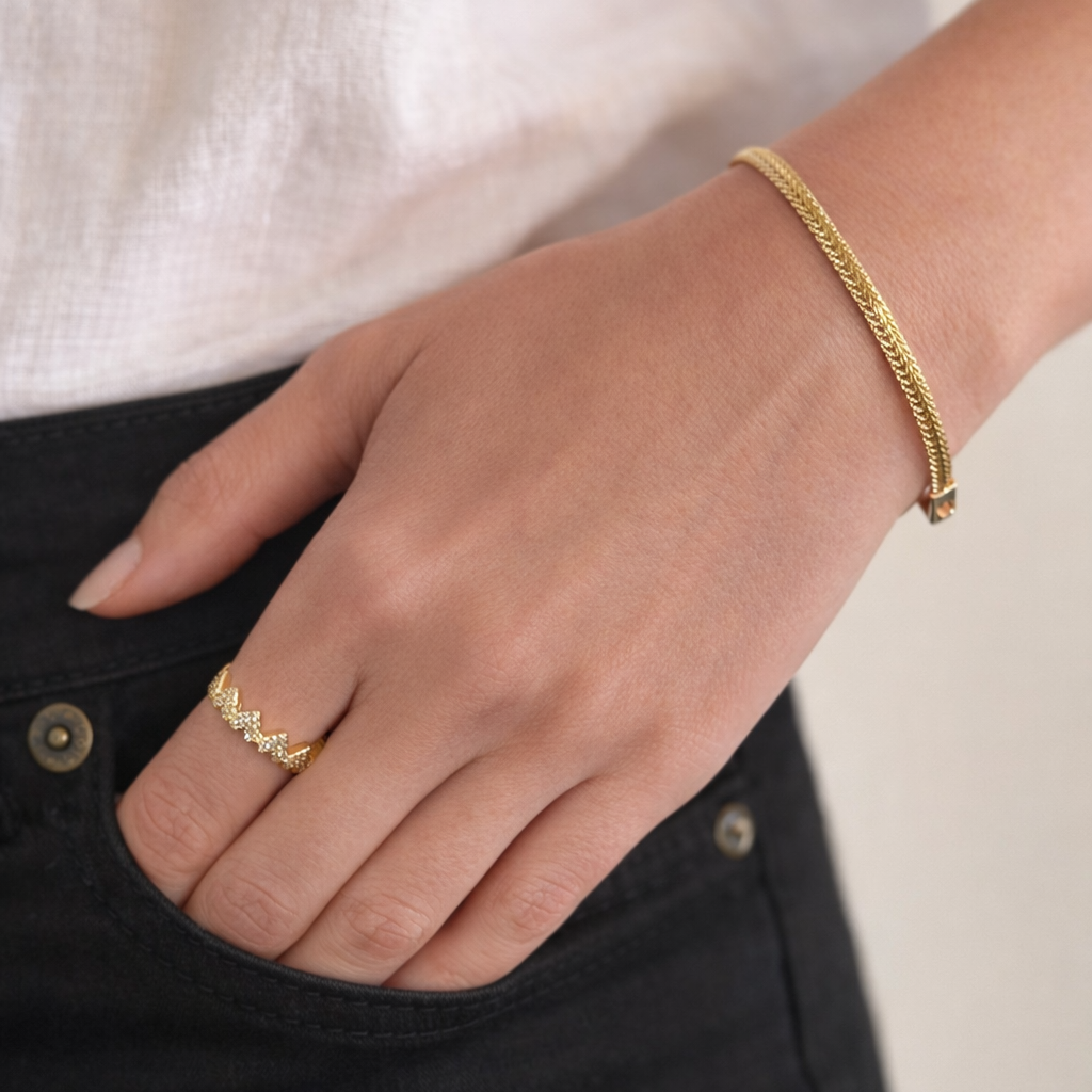 Gold bracelet and a heart-shaped ring with zirconia on a hand with a blurred background