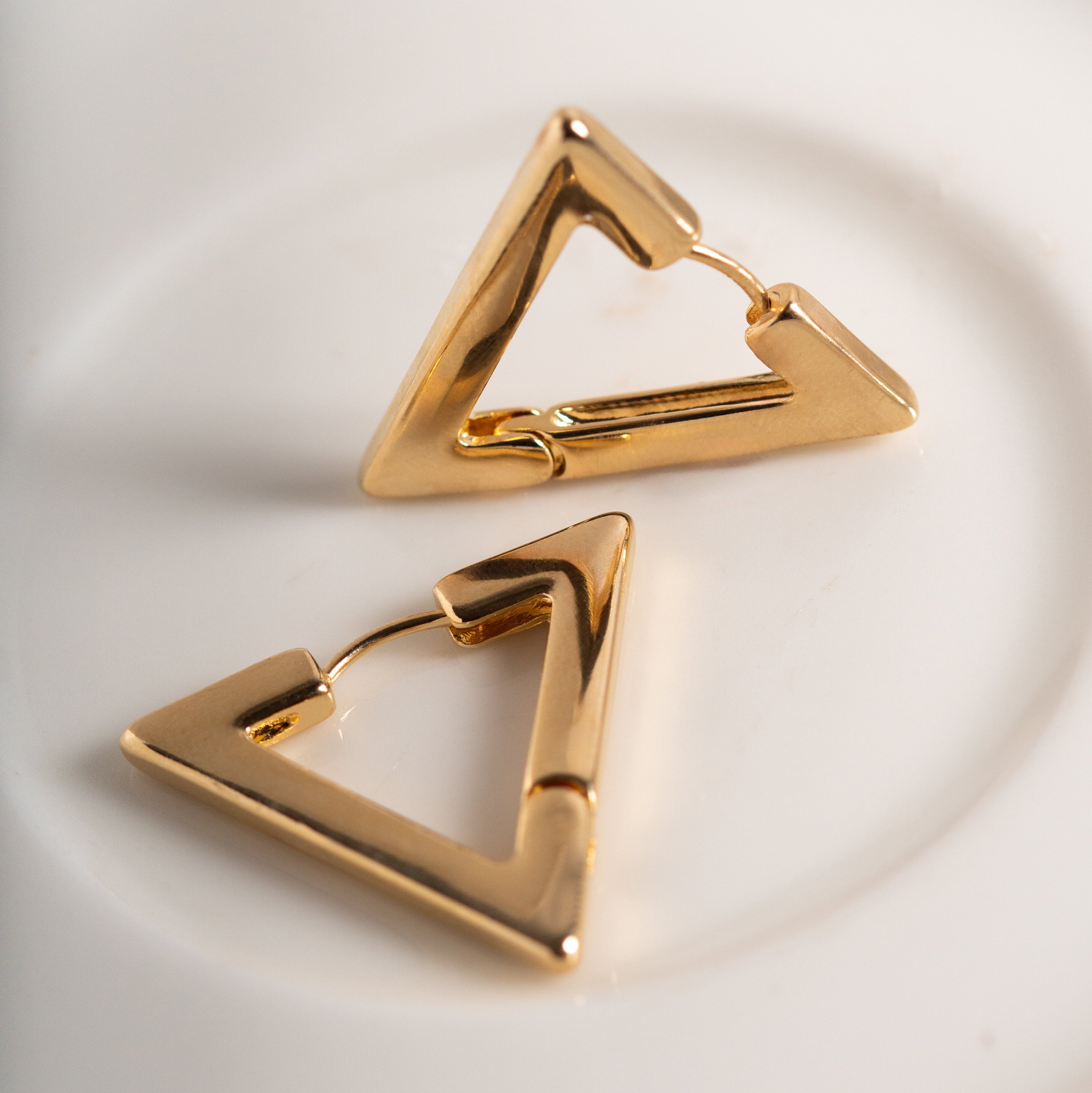 Gold triangle-shaped earrings on a light background
