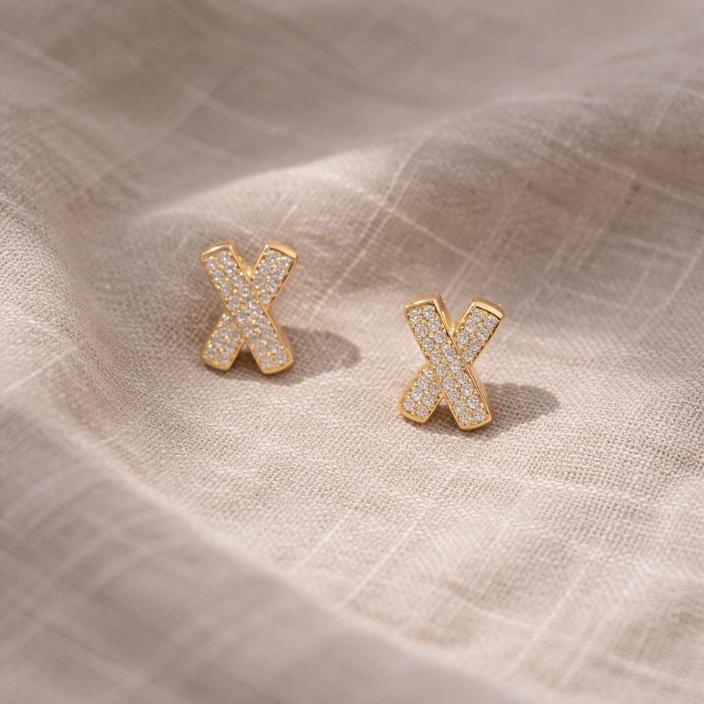 Gold 'X' earrings on a textured beige fabric background