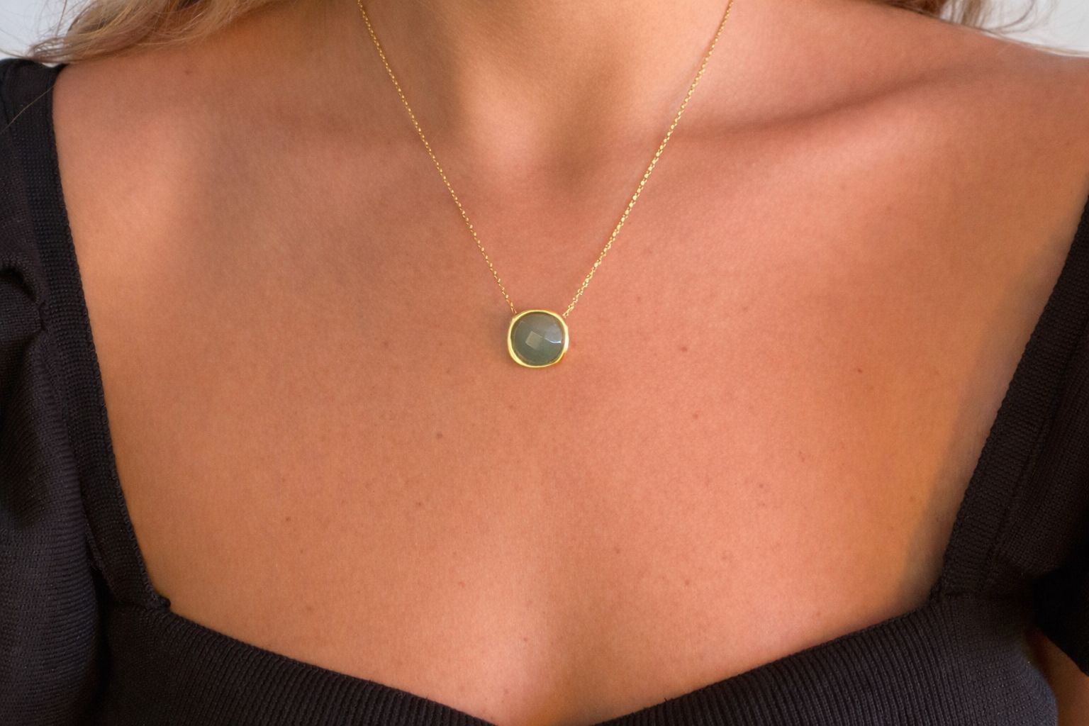 Necklace with a green pendant on a person wearing a black top